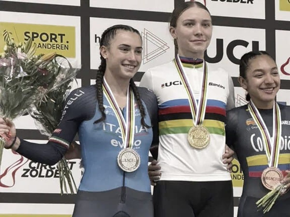 Ciclista colombiana en un velódromo de pista celebrando un podio mundial.