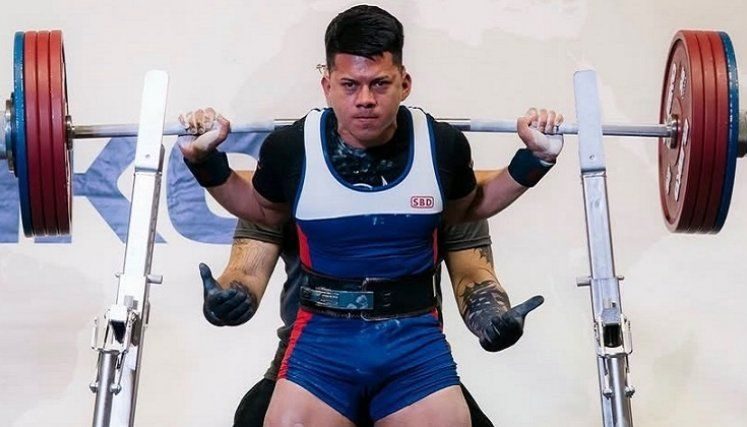 Levantador de potencia en una tarima de competencia con barra y discos.